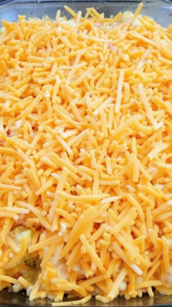 Unbaked cauliflower mixture in a 9x9 glass dish topped with shredded cheddar cheese, ready for baking