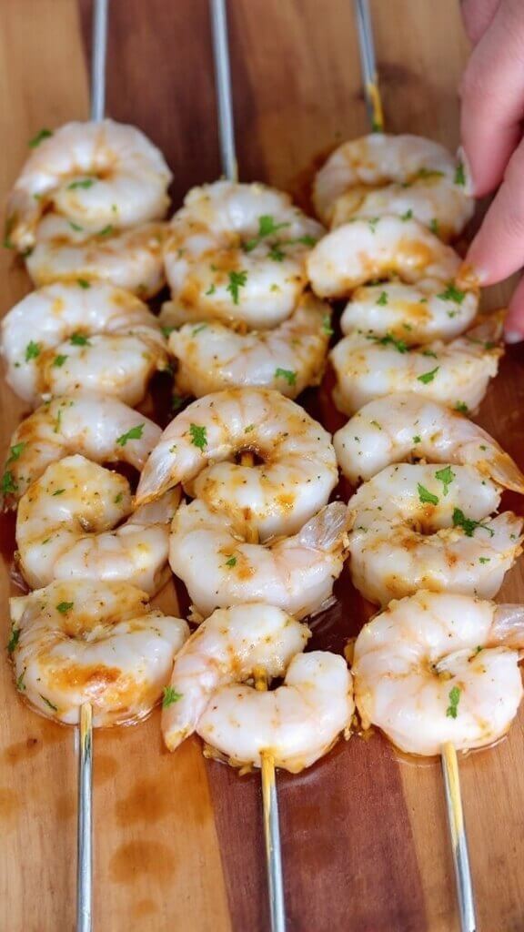 Perfect Grilled Shrimp Skewers 6 Marinated shrimp on metal skewers evenly space, coated with herbs, on a wooden cutting board