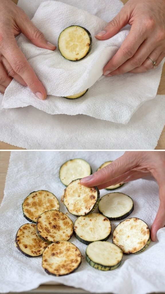 Hands pressing paper towels onto zucchini slices to absorb moisture, with dry zucchini rounds and damp paper towels in view