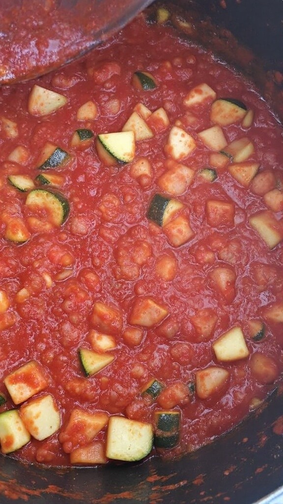 Marinara sauce and sausage mixture simmering in pan with chopped zucchini, displaying a rich red color and slight bubbling around edges