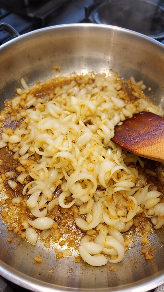 Walnut Taco &Quot;Meat&Quot; (Vegan, Gluten-Free Option) 5 Sautéed onions and garlic with golden brown edges in a large stainless steel skillet over flame, steam rising, with wooden spatula on pan edge