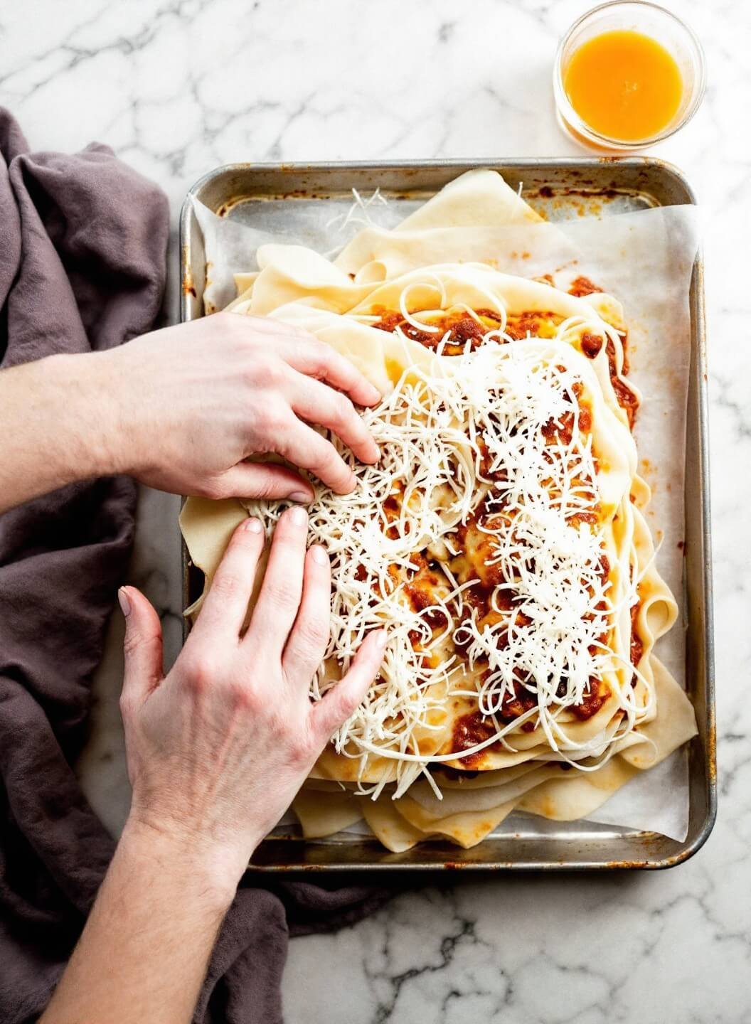 Two Easy Low-Carb Beef Lasagna Recipes: Eggplant &Amp; Cheese-Based 5 Hands assembling lasagna with steam rising from golden sauce during layering process, number 1253 in image sequence.