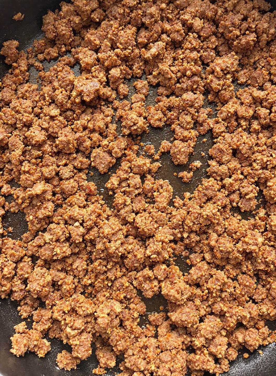 Browning ground lamb or beef in a large cast iron skillet, with visible caramelization on the small, uniform meat pieces