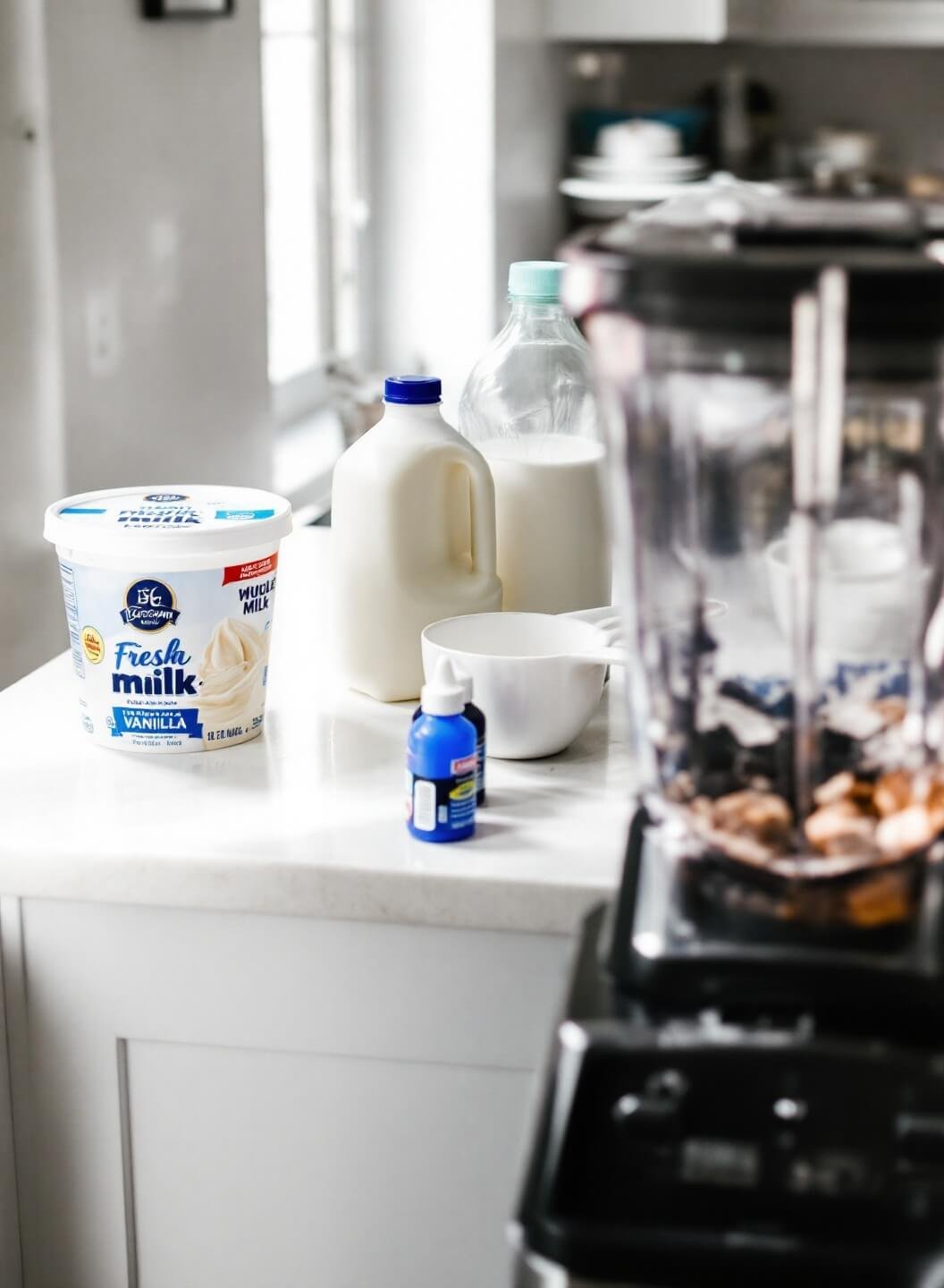Blue Milkshake Recipe 3 Ingredients for blue milkshake including vanilla ice cream, milk, extracts, and food coloring on a kitchen counter with a blender