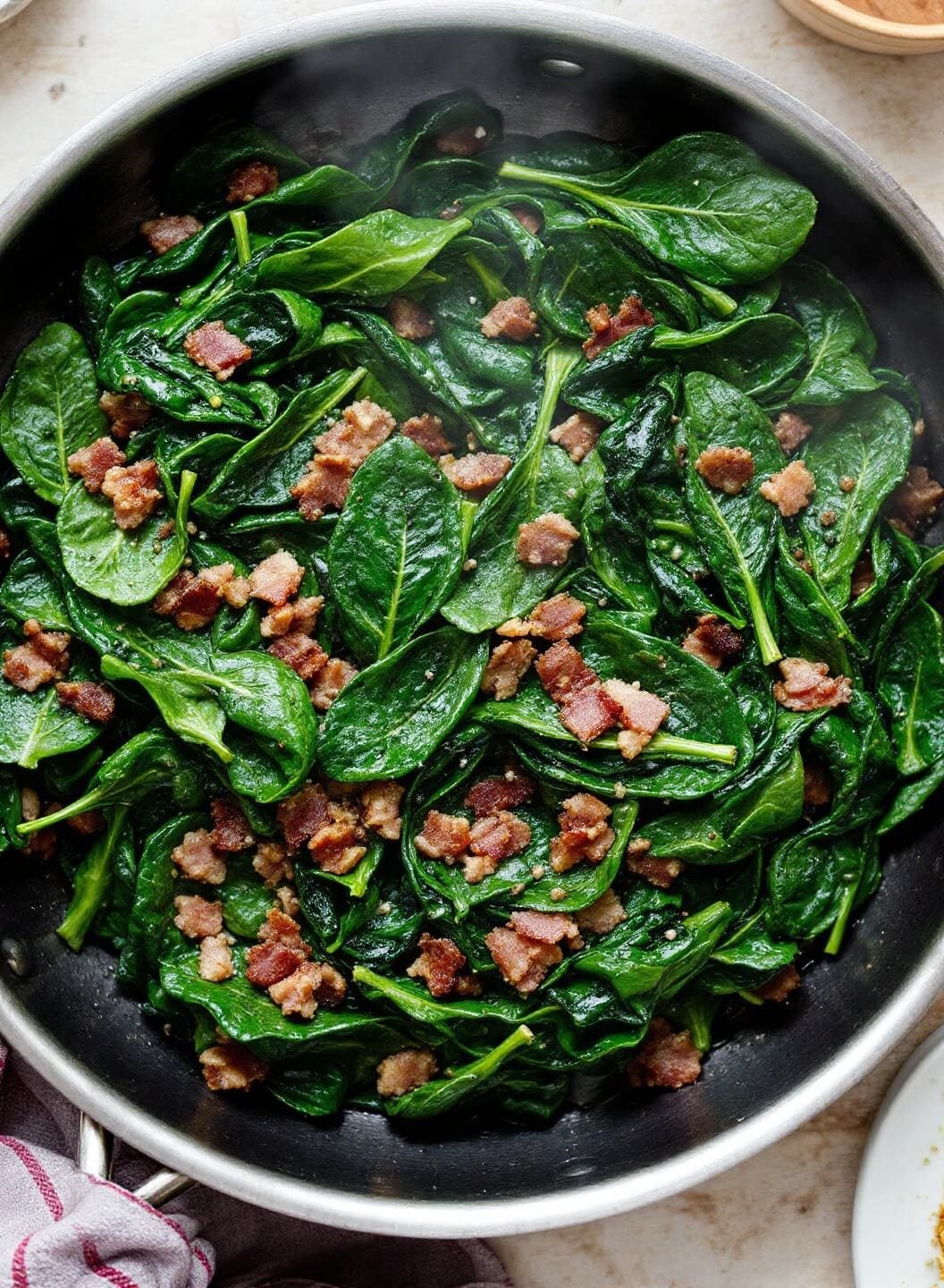 Savory Keto Breakfast Bowl 4 Steaming wilted spinach with bacon grease in a vintage pan on a rustic kitchen table.