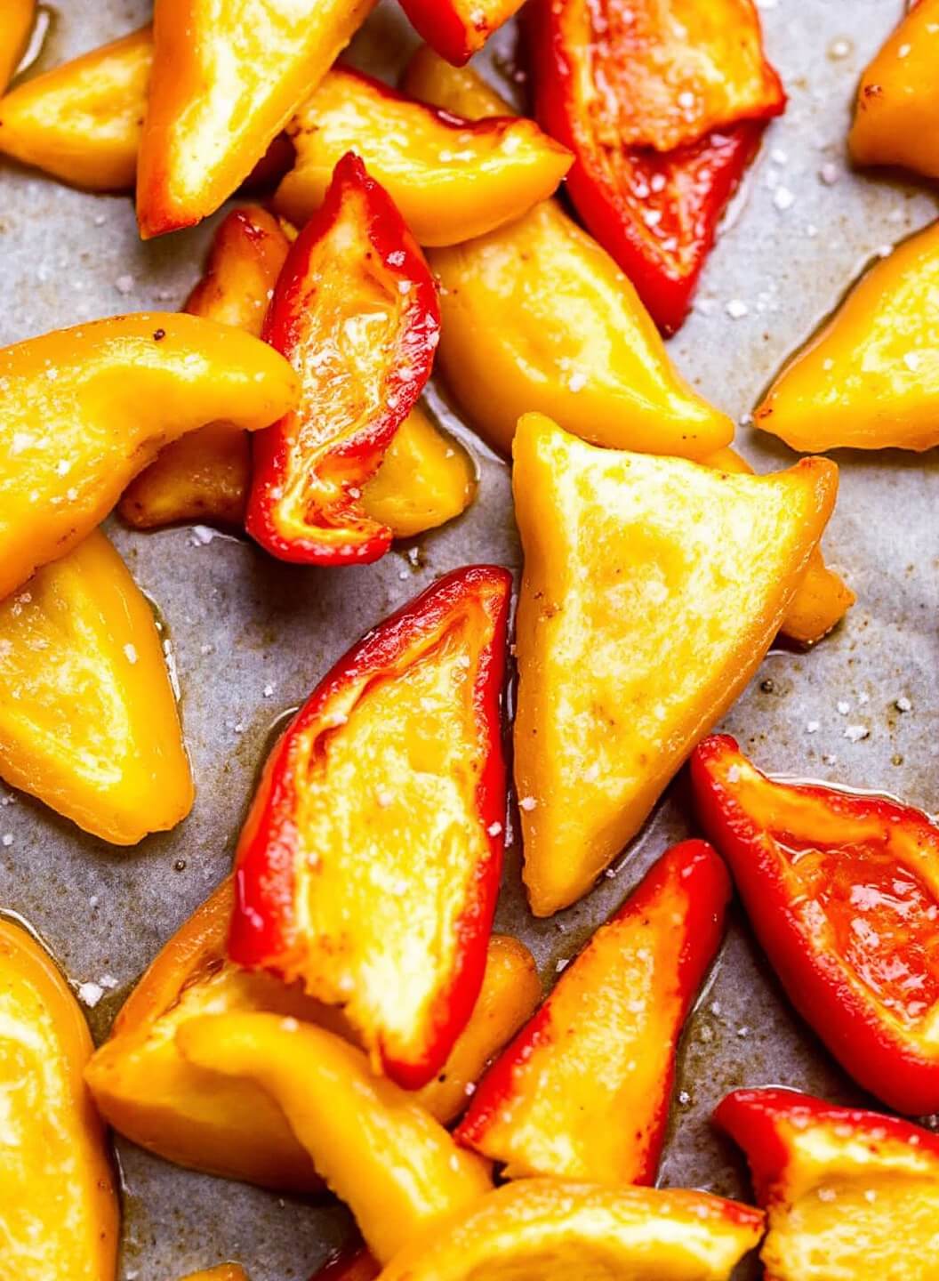 Sliced bell peppers on parchment-lined baking sheet resembling nacho chips, glistening with olive oil and sprinkled with sea salt crystals