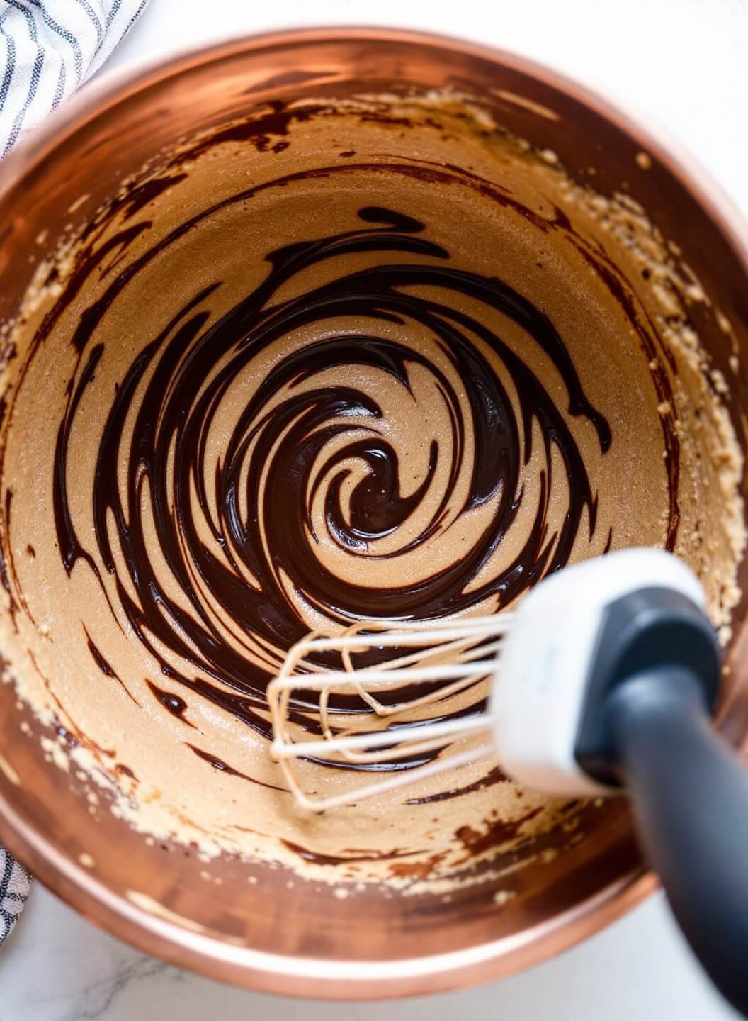 Mixing keto brownie batter with dark chocolate swirls in a vintage copper bowl