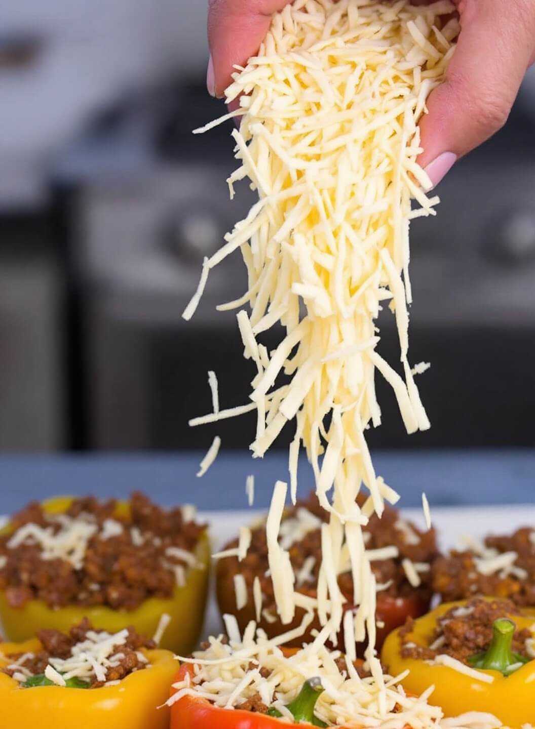 Shredded mexican cheese blend being sprinkled on meat-topped bell peppers
