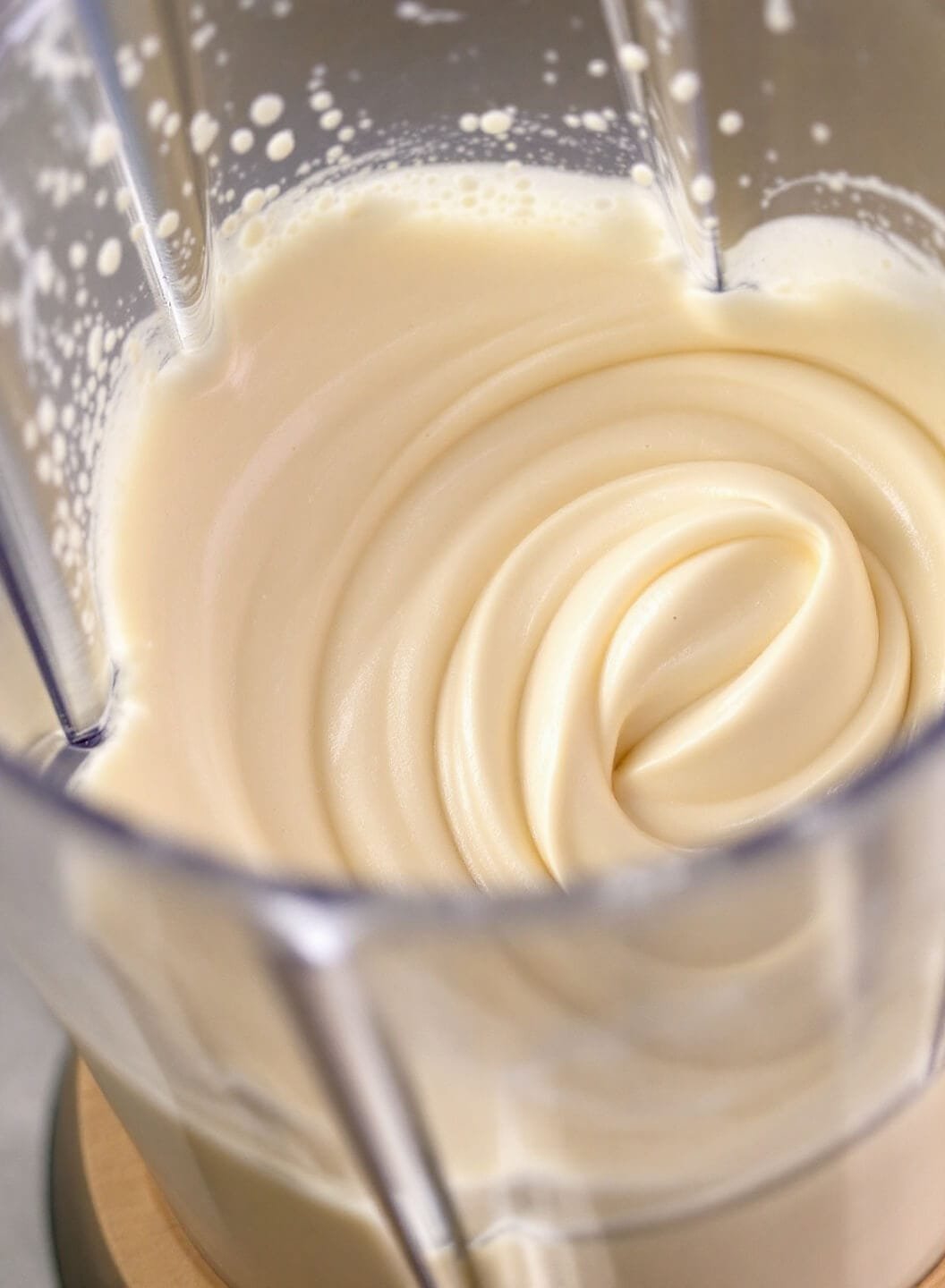 Close-up of a professional blender mixing cottage cheese and protein powder into a creamy substance, with dynamic air bubbles against a stainless steel backdrop.