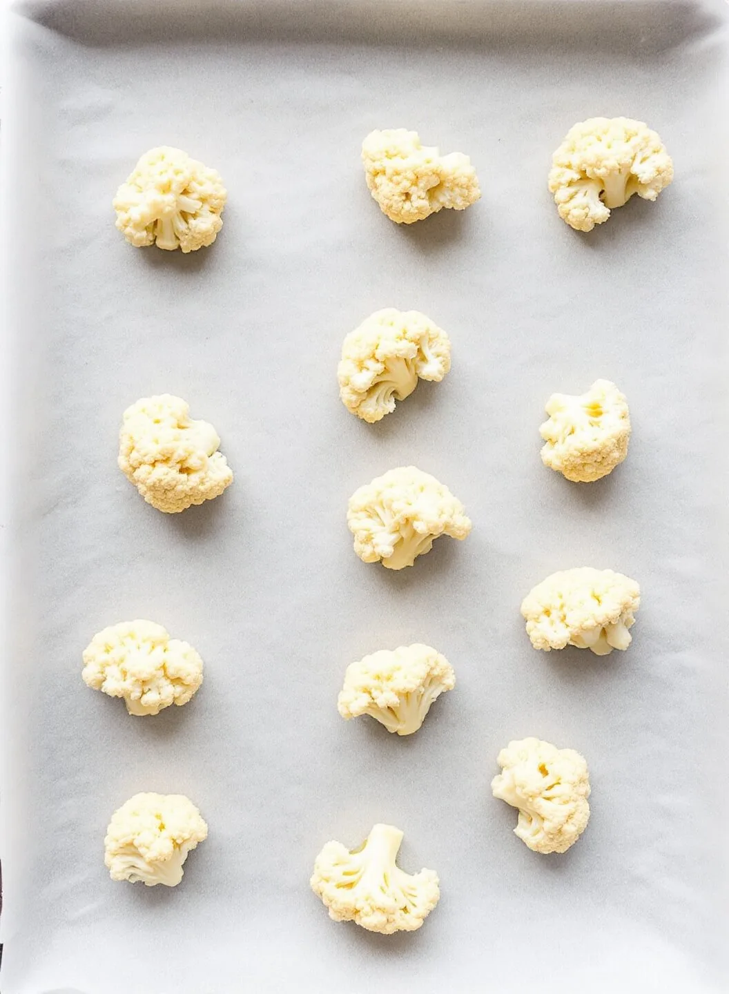 Crispy Garlic Parmesan Cauliflower Fries 6 Unbaked cauliflower florets arranged on parchment paper on a baking sheet.