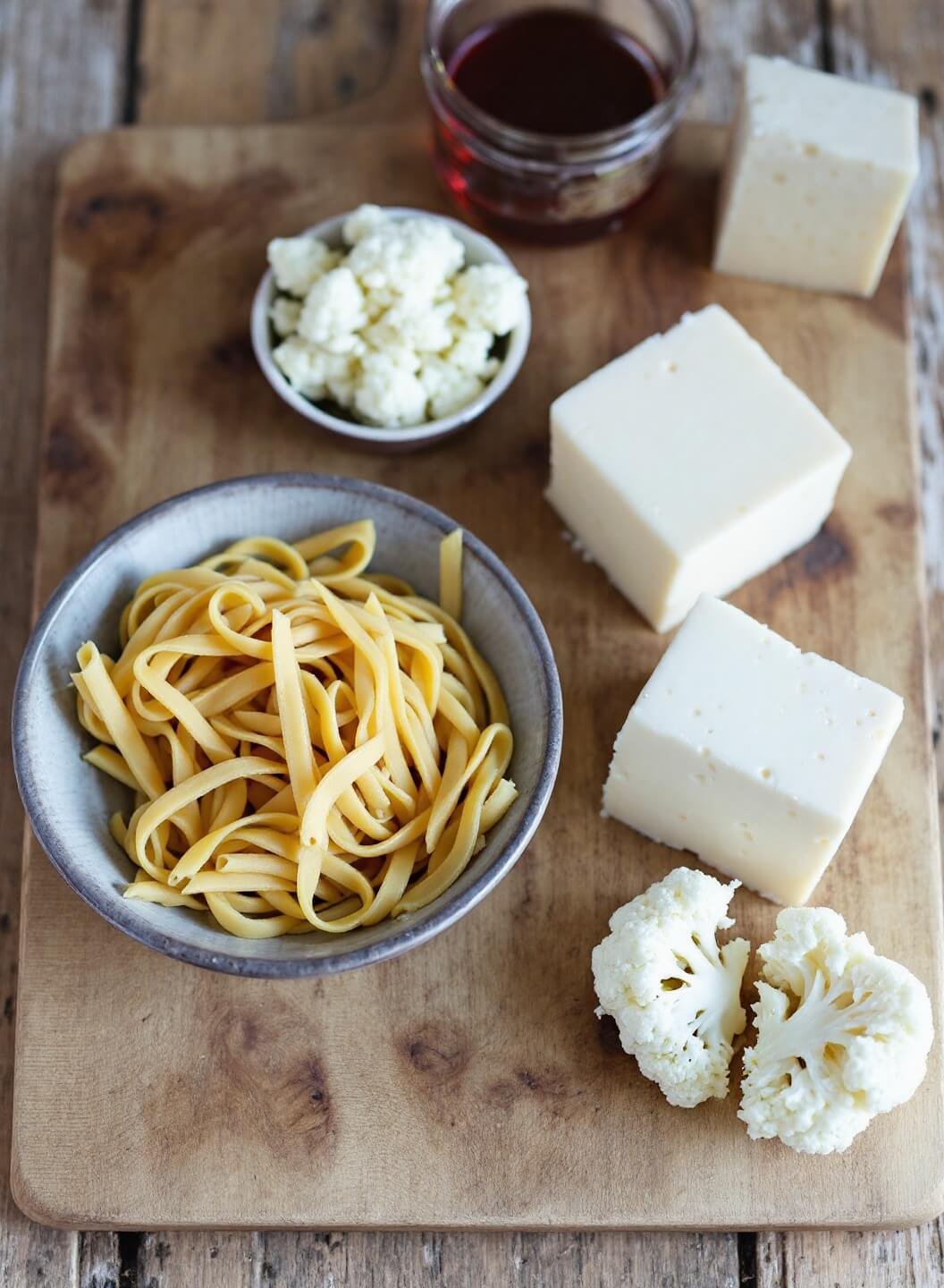 Baked Ziti With Cauliflower &Amp; Three Cheeses 3 Raw ingredients for pasta with cauliflower and three kinds of cheeses arranged on a rustic wooden board under natural lighting