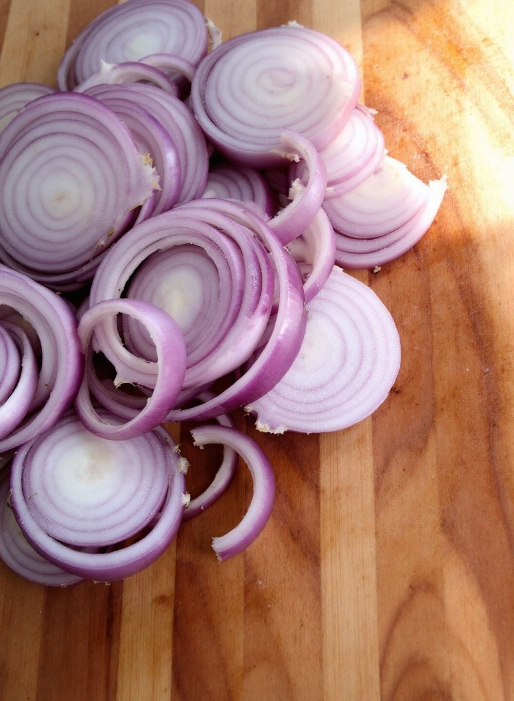 Classic French Onion Soup (Without Bread) 3 Sliced onions of even thickness on a wooden cutting board under natural lighting