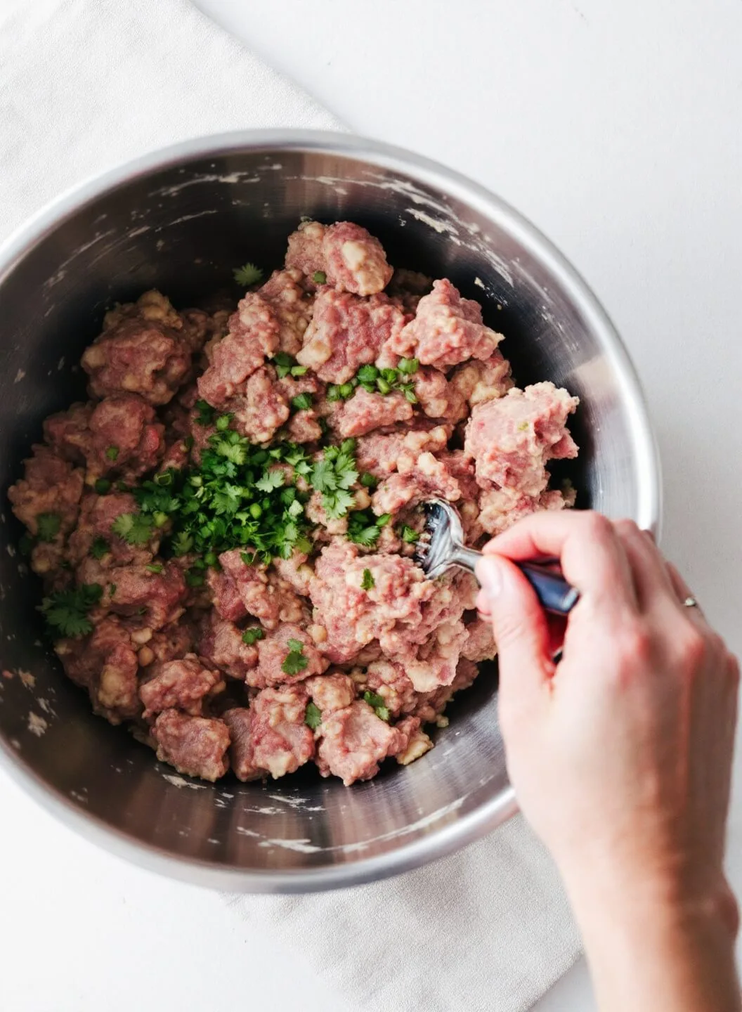 Bacon-Wrapped Keto Meatloaf 5 Hands gently mixing meat mixture in a steel bowl with ingredients marbled together