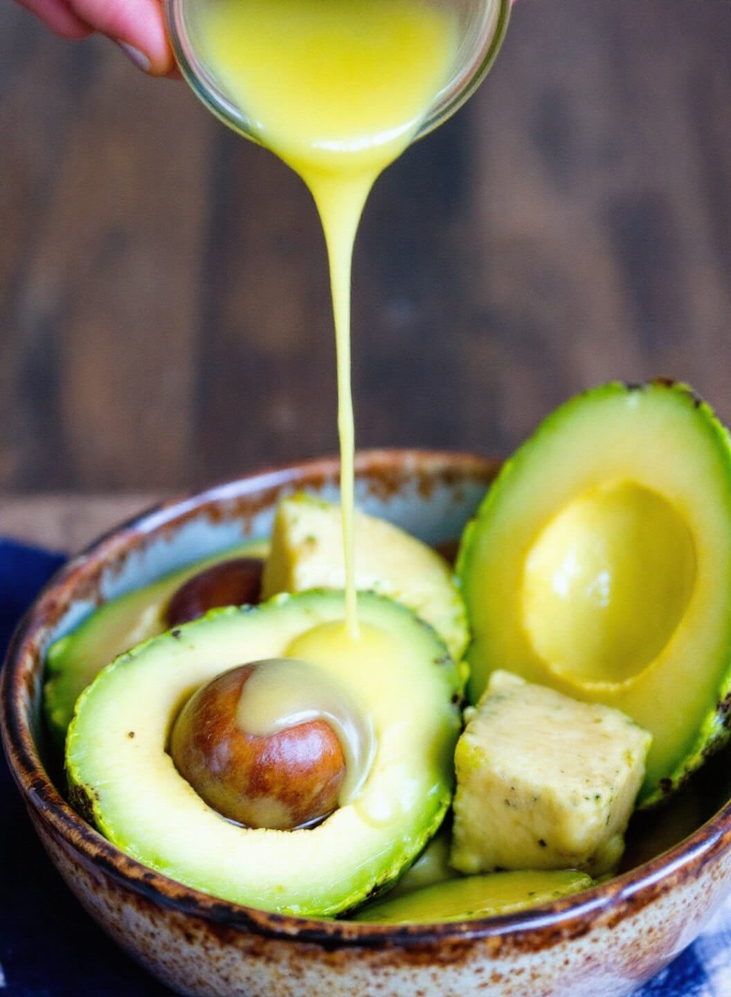 Easy Keto Guacamole (5-Minute Restaurant Style) 4 Person scooping halved avocados into a rustic ceramic bowl with a drizzle of lime juice