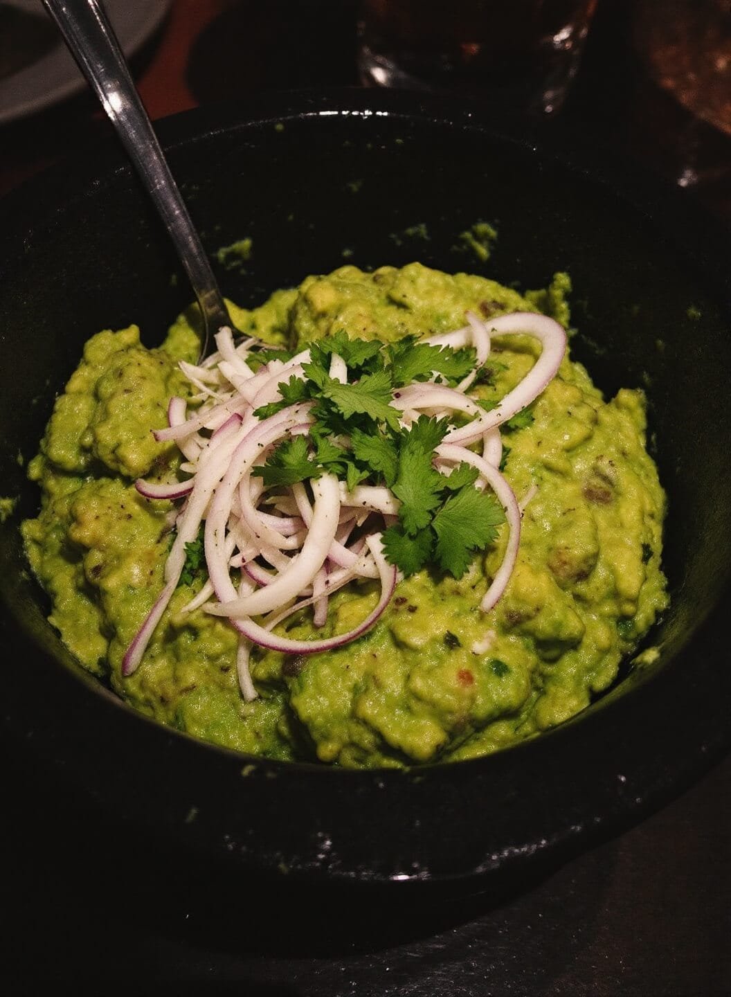 Easy Keto Guacamole (5-Minute Restaurant Style) 7 Guacamole served in a traditional molcajete, garnished with cilantro, in a dimly lit restaurant setting