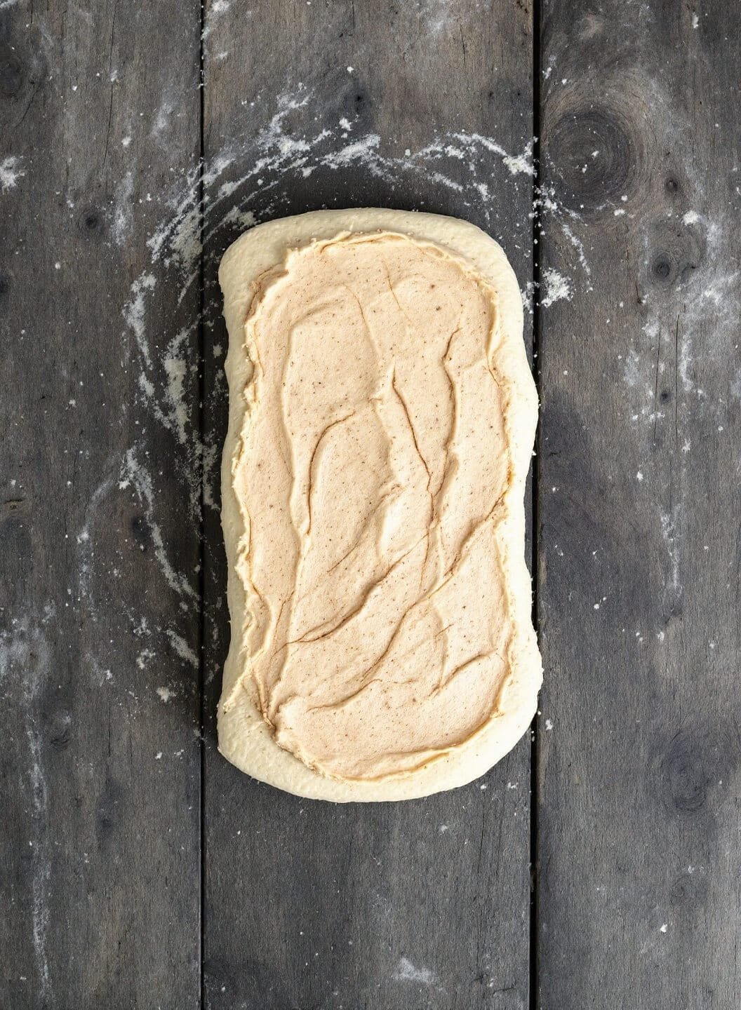Keto Cinnamon Rolls (Fathead Dough) 5 Cinnamon butter spread on rectangular dough on a rustic wooden surface