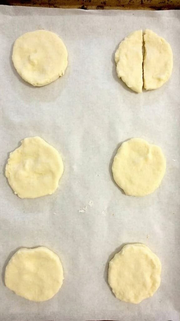 Portioned raw biscuit dough evenly spaced on a parchment lined baking sheet