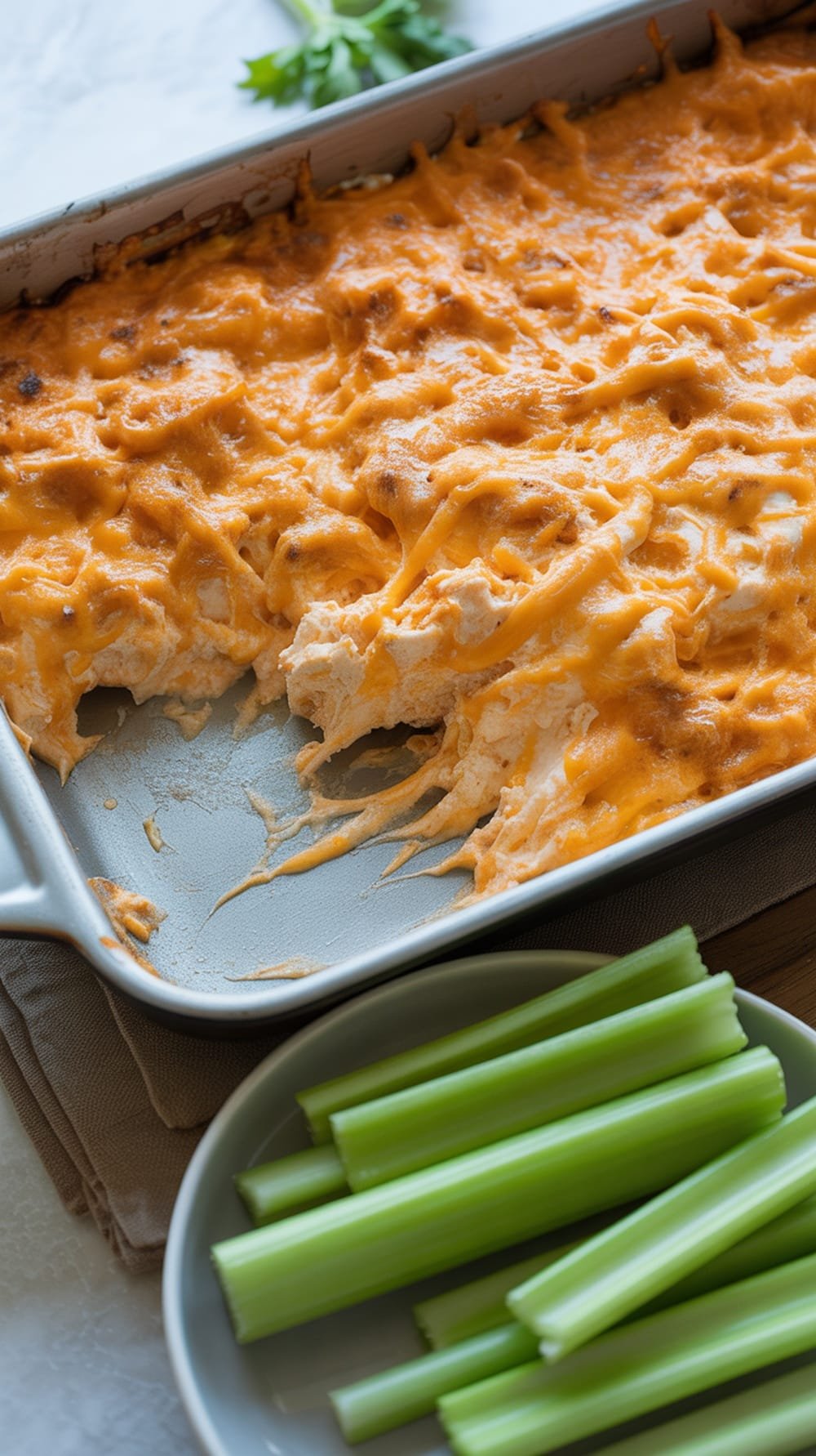Buffalo chicken dip with melted cheese and celery sticks on the side.